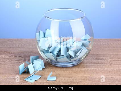 Stücke Papier für Lotterie in Vase auf Holztisch auf blauem Hintergrund Stockfoto