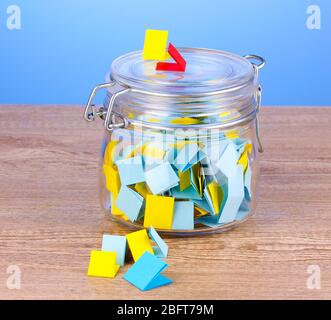 Stücke Papier für Lotterie in Glas auf Holztisch auf blauem Hintergrund Stockfoto