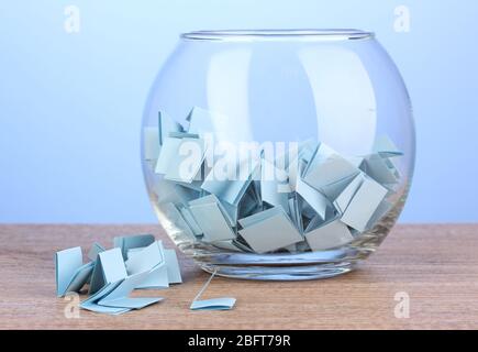 Stücke Papier für Lotterie in Vase auf Holztisch auf blauem Hintergrund Stockfoto