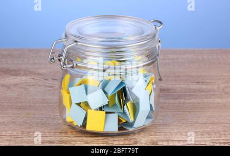 Stücke Papier für Lotterie in Glas auf Holztisch auf blauem Hintergrund Stockfoto
