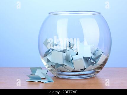 Stücke Papier für Lotterie in Vase auf Holztisch auf blauem Hintergrund Stockfoto