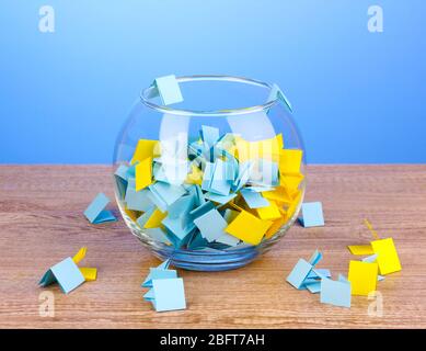 Stücke Papier für Lotterie in Vase auf Holztisch auf blauem Hintergrund Stockfoto