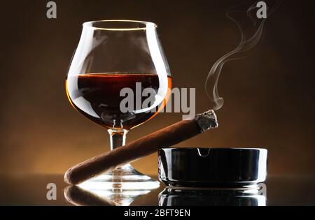 Glas Brandy und Zigarre auf braunem Hintergrund Stockfoto