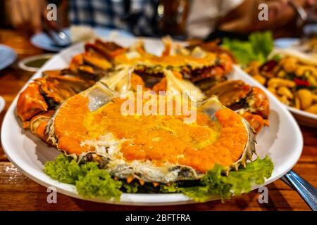 Gedämpfte Eierkrabbe mit Krallen und Gemüse in weißer Schüssel auf einem Holztisch. Stockfoto