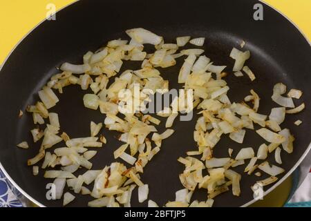 Nahaufnahme von sautierten gehackten frischen gelben Zwiebeln in der Antihaft-Pfanne Stockfoto