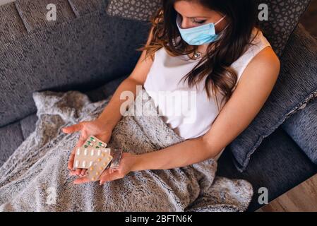 Eine schöne kaukasische kranke Frau mit einer Maske auf ihr Gesicht und Pillen in der Hand liegen auf dem Bett Stockfoto