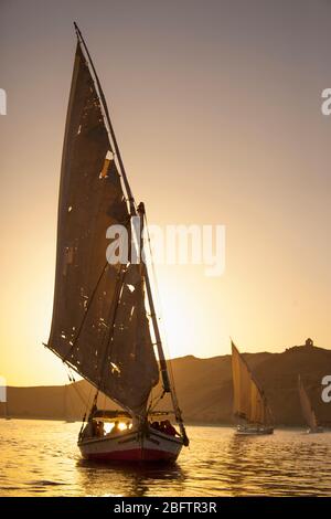 Ein Felucca Segelboot ist bei Sonnenuntergang auf dem Nil in Assuan, Ägypten, silhouettiert. Stockfoto