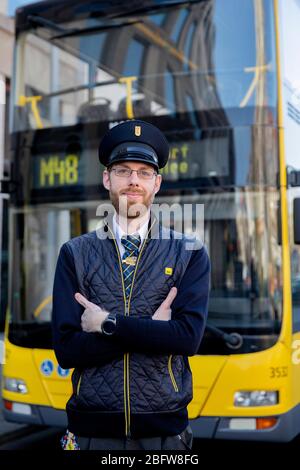 06. April 2020, Berlin: Marcel Kohlschmidt, Busfahrer, schaut in die Kamera des Fotografen. Der 28-Jährige sagt, dass es weniger Verkehr auf den Straßen, weniger Passagiere und gelegentlich eine gruselige Stille gebe. Der Vordereingang ist blockiert, eine Folie schützt den Fahrer vollständig vor dem Passagierbereich und Fahrkarten werden nicht mehr im Bus verkauft. Er glaubt bereits, dass einige Leute nutzen diese, um schwarz zu fahren, vor allem, da die Ticketeinnahmen um 95 Prozent gesunken sind. Wird ein Rollstuhlfahrer in den Bus eingeladen, schützt er sich mit Maske und Handschuhen. Kohlschmidt ist weniger besorgt Stockfoto