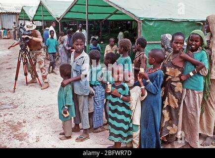 1993 - Der Chief Fotograf Mate Robert Sasek Videobänder Somalis Futter für eine Mahlzeit an der Sorge der Fütterung während der multinationalen Entlastung Bemühung Operation Restore Hope. Das Zentrum wird von der irischen Hilfsorganisation Sorge betrieben. Stockfoto