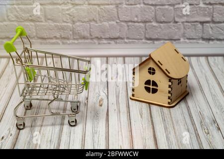 Warenkorb mit grünem Griff und Holzhaus auf dem Tisch Stockfoto
