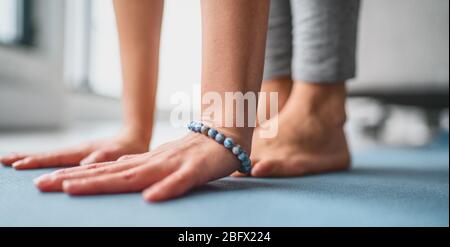 Yoga im Fitnessstudio - Yogalehrer Stretching in der Vinyasa Yoga-Klasse. Nahaufnahme der Hände mit blauem mala-Armband und barfuß Füße zu Hause. Stockfoto