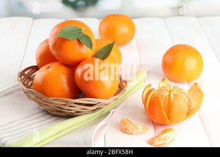 Mandarinen mit Blättern in einem schönen Korb, auf weißem Holztisch Stockfoto