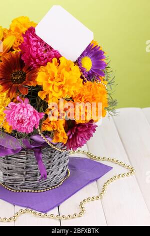 Schöner Strauß von hellen Blumen mit Papiernote auf Holztisch auf grünem Hintergrund Stockfoto