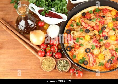 Bunte Komposition aus köstlichen Pizza, Gemüse und Gewürze auf Holzhintergrund Nahaufnahme Stockfoto