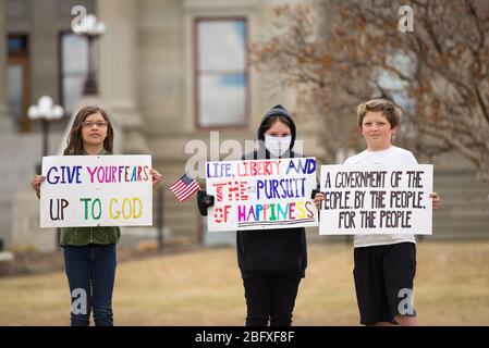 Helena, Montana - 19. April 2020: Kinder stehen vor dem Kapitolgebäude des Staates und halten maskierte Schilder, um gegen die Schließung der Regierung zu protestieren Stockfoto