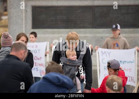 Helena, Montana - 19. April 2020: Mann und Vater küssen Baby auf Kopf während sie bei einem Protest über den Aufenthalt in der Heimat Befehle und Regierungsstillstand beten Stockfoto