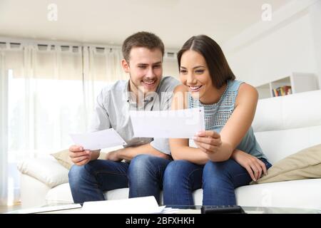 Ein glückliches junges Paar, das zu Hause auf einer Couch nach Rechnungen sucht und sie überprüft Stockfoto