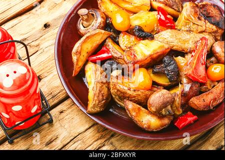 Gebackene hausgemachte Kartoffeln mit Champignonpilzen. Bratkartoffeln auf einem hölzernen Vintage Hintergrund. Stockfoto