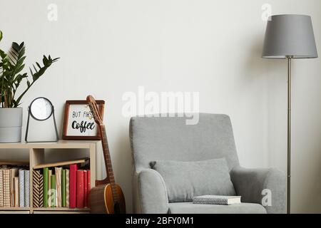Hintergrundbild mit gemütlicher, moderner Innenausstattung mit minimalem Dekor und grauem Sessel an weißer Wand, Kopierraum oben Stockfoto