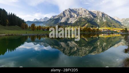 Ruhige Alpenlandschaft mit Wasserspiegelung und typisch österreichischem Dorf im Hintergrund Stockfoto