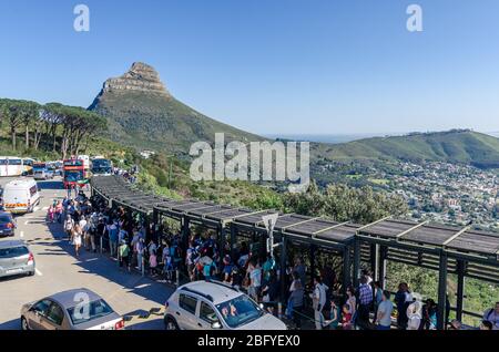 Eine große Menge Touristen, die sich für Tickets an der Seilbahn Table Mountain anstellen, mit Löwen, die im Hintergrund Kapstadt, Südafrika, fahren Stockfoto