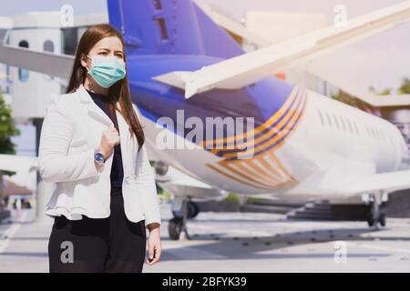 Die Geschäftsfrau lächelt und trägt eine Schutzmaske gegen Coronavirus, PM 2.5 und Kälte vor dem Flugzeug. Coronavirus und Air pol Stockfoto