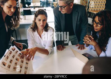 Kreatives Start-up-Team diskutiert Ideen in einem Meeting. Gruppe von multiethnischen Personen während eines Geschäftstreffens, die sich ein Kontaktblatt mit Fotos anschauen. Stockfoto