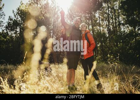 Mann zeigt Frau etwas, während sie durch einen Wald geht. Pärchen auf Campingreise mit Blick auf die Aussicht. Stockfoto