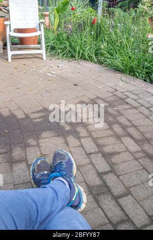 Gekreuzte Beine mit Füßen in alten Turnschuhen isoliert auf einer gepflasterten Oberfläche im Freien Bild im vertikalen Format Stockfoto