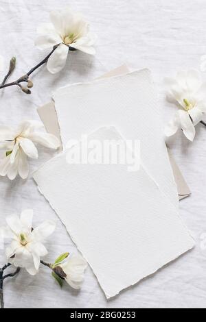 Hochzeitspapier-Set. Mock-up-Szene mit leeren Papier Grußkarten, Umschlag auf Leinen Tischdecke Hintergrund. Weiße Magnolia stellata Äste, Stockfoto