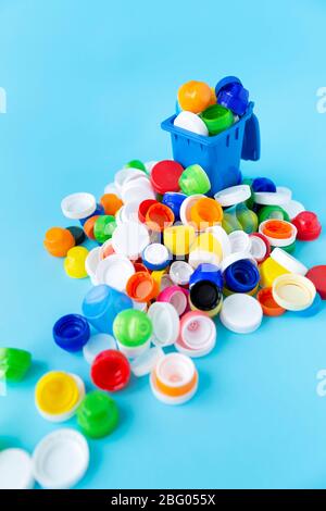 Miniatur-Recycling-Behälter mit Kunststoffflaschen Kappen in verschiedenen Größen, Formen und Farben auf hellblauem Hintergrund gefüllt. Kunststoffrecycling-Konzept Stockfoto