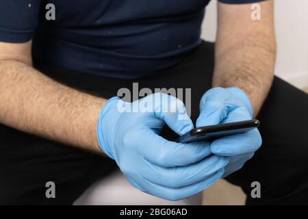 Die Hände eines Mannes mit Handschuhen, die ein Mobiltelefon benutzen Stockfoto