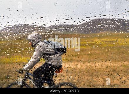 Bei Regen fällt und man am Mountainbike Touren auf der Landstraße aus Fenster Focus. Stockfoto