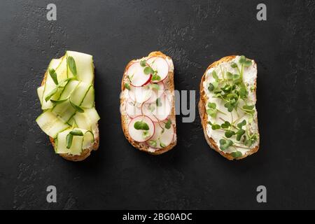 Sandwiches mit allerlei Tomaten, frischem Rettich, Microgreens, Frischkäse auf schwarzem Stein Hintergrund. Draufsicht. Stockfoto