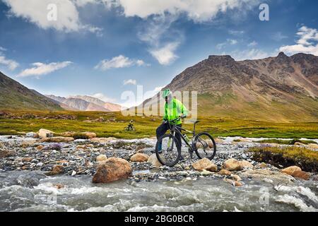 Mann mit dem Mountainbike über den Fluss in die wilden Berge gegen bewölkter Himmel Hintergrund. Stockfoto