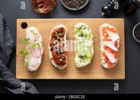 Hausgemachte Sandwiches auf Toast mit frischem Gemüse, Radieschen, Tomaten, Gurken und Mikrogreens und Zutaten auf schwarzem Hintergrund. Blick von oben Stockfoto