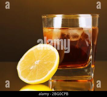 Glas Whiskey mit Eis und Zitrone auf gelbem Hintergrund Stockfoto