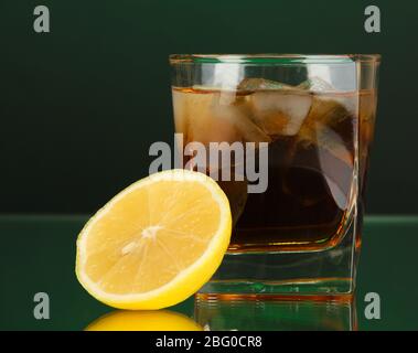 Glas Whisky mit Eis und Zitrone auf grünem Hintergrund Stockfoto