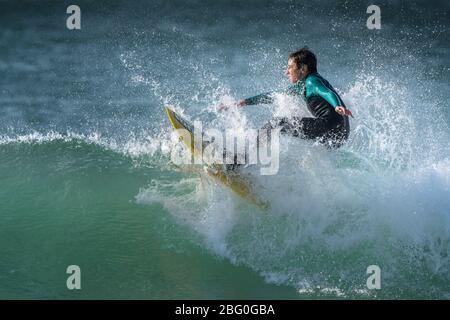 Spektakuläre Surferaction, während ein junger Surfer eine Welle im Fistral in Newquay in Cornwall reitet. Stockfoto