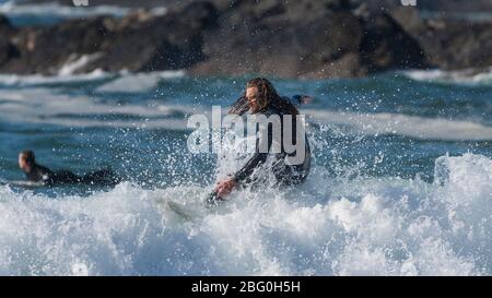 Ein Panoramabild eines männlichen Surfers mit langen Haaren, der eine Welle bei Fistral in Newquay in Cornwall reitet. Stockfoto