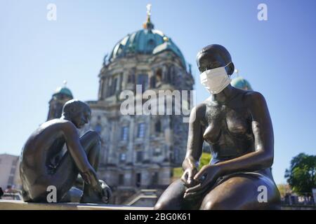 Berlin, Deutschland. April 2020. ILLUSTRATION - EINE Figur der Skulptur "drei Mädchen und ein Junge" des Künstlers Wilfried Fritzenreiter an der Spree trägt einen Mundschutz. Quelle: Jörg Carstensen/dpa/Alamy Live News Stockfoto