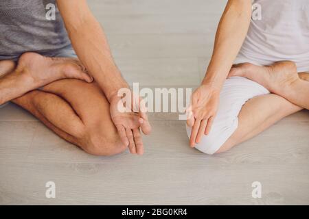 Entspannte Männer und Frauen meditieren in Lotusposition, während sie Yoga gemeinsam im hellen Raum zu Hause praktizieren Stockfoto