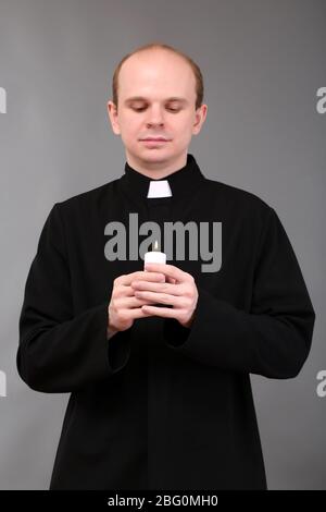 Portrait des jungen Pastors, der Kerze in der Hand hält, auf grauem Hintergrund Stockfoto