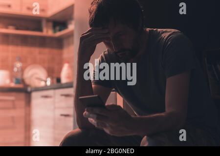 Depressiver Mann, der SMS auf dem Mobiltelefon in einem dunklen Raum eingibt, selektiver Fokus Stockfoto