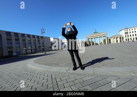 Berlin, Deutschland. April 2020. Eine junge Frau mit Mundschutz steht auf dem fast menschenleeren Pariser Platz vor dem Brandenburger Tor und nimmt die Situation mit ihrem Handy auf. Der ansonsten sehr belebte Platz mitten in der Hauptstadt wird durch die andauernde Corona-Pandemie verwaist. Quelle: Wolfgang Kumm/dpa/Alamy Live News Stockfoto