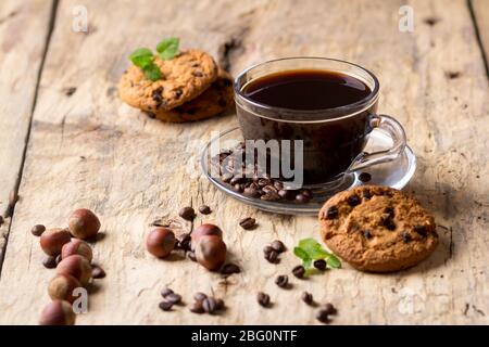 Schwarzer Kaffee in einer Glasbecher mit Kaffeebohnen. In der Nähe von Cookies und Haselnüssen Stockfoto