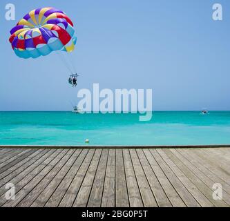 Leere Holzplattform neben dem tropischen Strand in Punta Cana, Dominikanische Republik. Bunte Parasailflügel fliegen über türkisblaues Wasser des Sargasso Meer in t Stockfoto