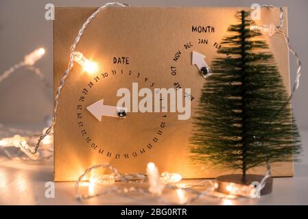Nahaufnahme eines Pappkalenders, der am 25. Dezember mit Weihnachtslichtern und einer kleinen Kiefer im Vordergrund aufgestellt wurde. Chistmas Konzept. Stockfoto