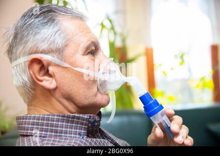 Leitender Mann, der medizinische Geräte für die Inhalation mit Atemschutzmaske verwendet, Vernebler im Zimmer Stockfoto