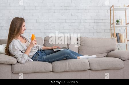 Junge Frau arbeitet am Laptop und trinkt frische orangen Detox Stockfoto
